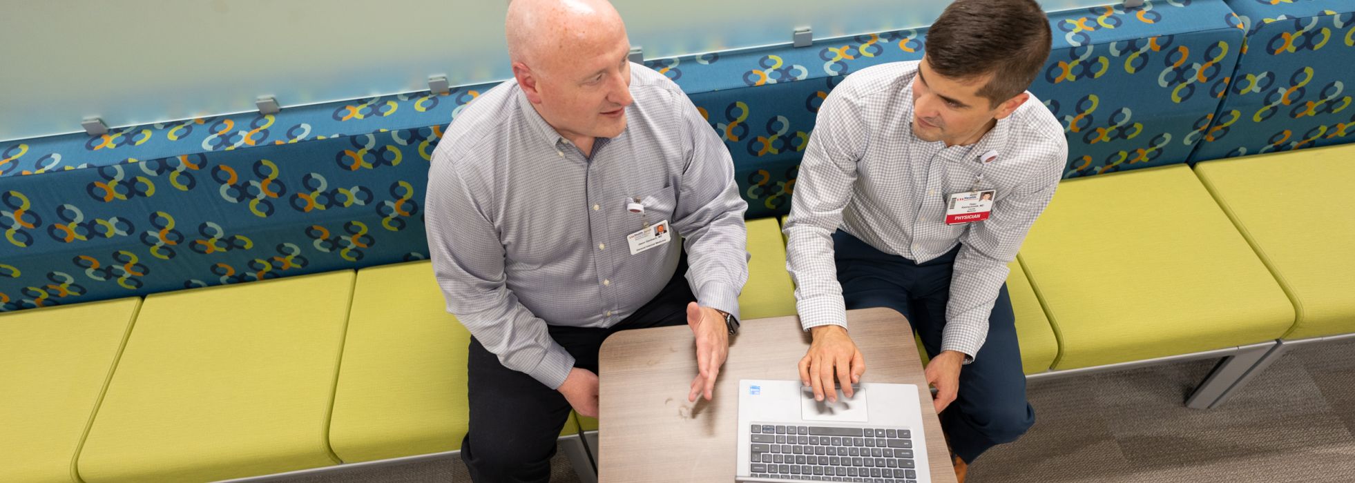 Photo looking down of Drs. Jason Dambach and Peter Kleinschmidt sitting on a yellow bench working on a laptop