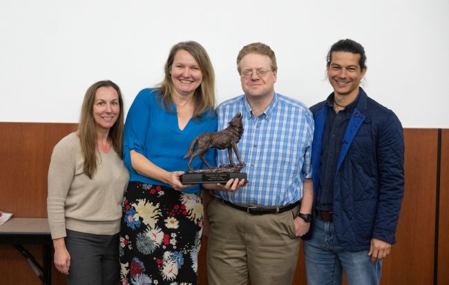Two women and two men stand holding a trophy shaped like a howling wolf