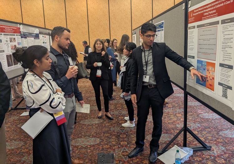 An internal medicine resident discusses his conference poster with onlookers.