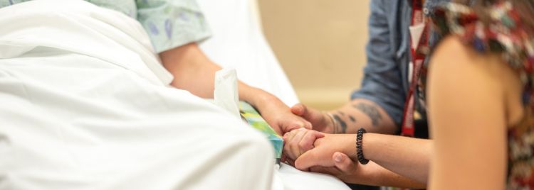 Patient in hospital bed, holding hands with loved ones.