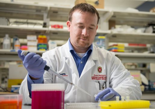 Dr. Dustin Deming in a lab in a white coat holding a pipette